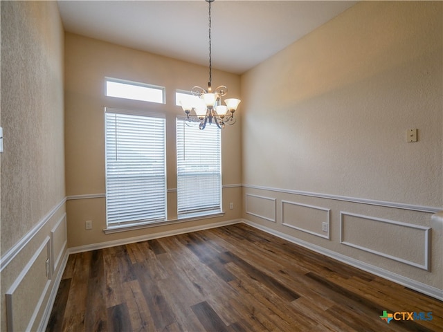 spare room with a chandelier and dark wood-type flooring