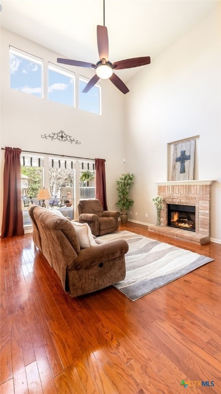 living room with a high ceiling, hardwood / wood-style flooring, a brick fireplace, and ceiling fan