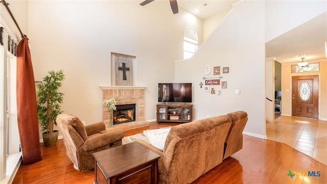 living room featuring a fireplace, a high ceiling, ceiling fan, and wood-type flooring