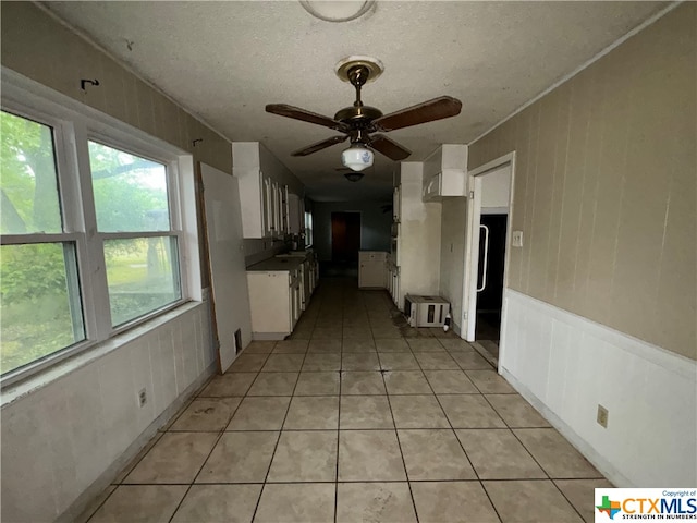 interior space featuring ceiling fan, white cabinets, light tile patterned flooring, and a textured ceiling