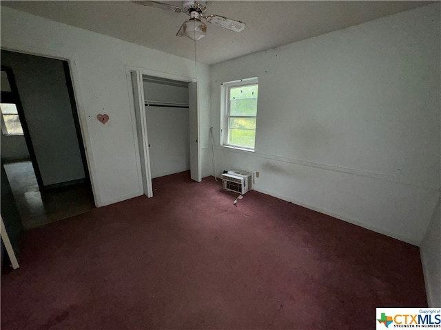 unfurnished bedroom featuring dark colored carpet, a closet, a wall mounted air conditioner, and ceiling fan