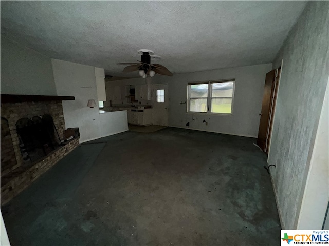 unfurnished living room featuring ceiling fan, concrete floors, a textured ceiling, and a brick fireplace