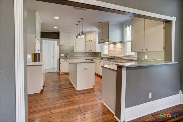 kitchen featuring kitchen peninsula, decorative light fixtures, hardwood / wood-style floors, a kitchen island, and white cabinets