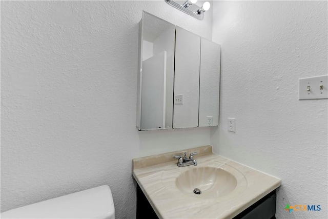 half bath featuring vanity, toilet, and a textured wall