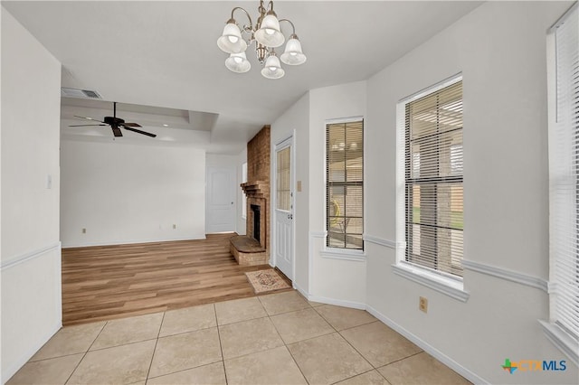 interior space with light tile patterned flooring, a large fireplace, ceiling fan with notable chandelier, visible vents, and baseboards