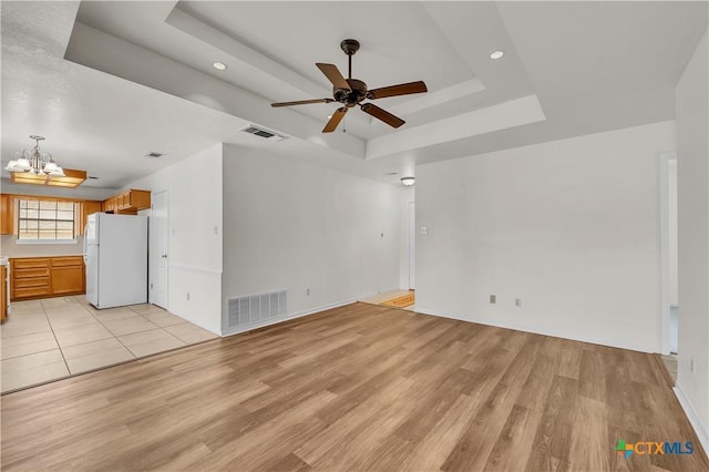 unfurnished living room featuring light wood finished floors, visible vents, a raised ceiling, and ceiling fan with notable chandelier