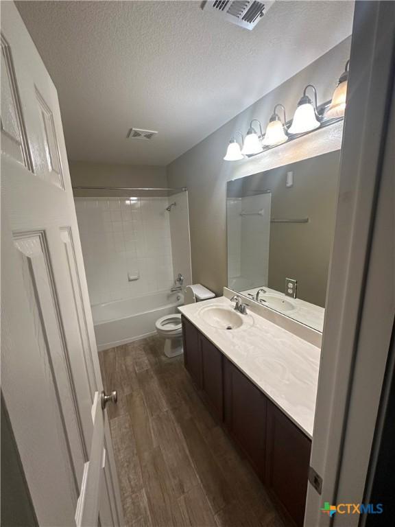 full bathroom with wood-type flooring, vanity, toilet, a textured ceiling, and washtub / shower combination