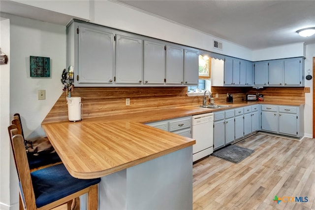 kitchen featuring backsplash, sink, dishwasher, kitchen peninsula, and light hardwood / wood-style flooring