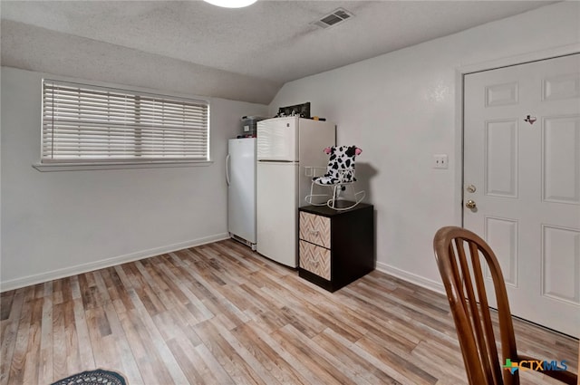 kitchen with white refrigerator, lofted ceiling, a textured ceiling, and light hardwood / wood-style flooring