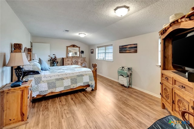 bedroom featuring light hardwood / wood-style floors, a textured ceiling, and vaulted ceiling