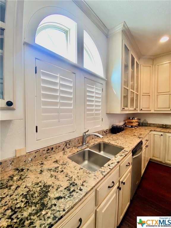 kitchen with light stone counters, ornamental molding, sink, dark wood-type flooring, and stainless steel dishwasher