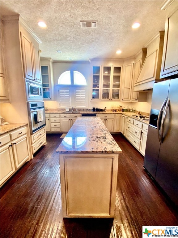 kitchen with dark hardwood / wood-style flooring, light stone counters, a center island, a textured ceiling, and appliances with stainless steel finishes