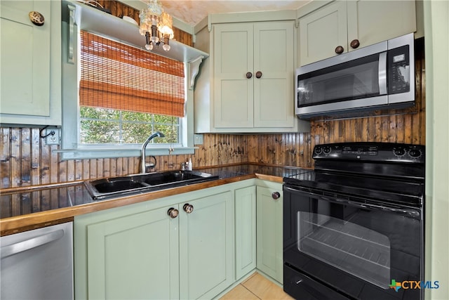 kitchen with light tile patterned flooring, green cabinets, sink, appliances with stainless steel finishes, and an inviting chandelier