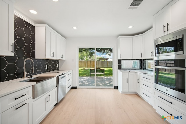 kitchen featuring sink, stainless steel appliances, light stone counters, light hardwood / wood-style flooring, and white cabinets