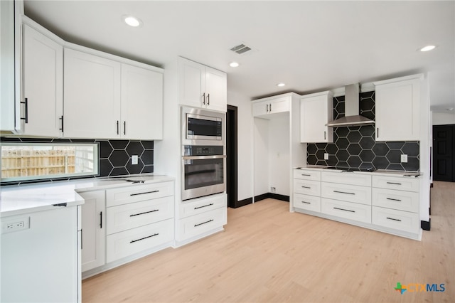 kitchen featuring white cabinetry, stainless steel appliances, wall chimney range hood, and light hardwood / wood-style floors