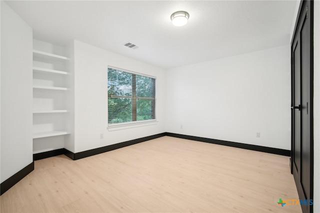 spare room with built in shelves and light wood-type flooring