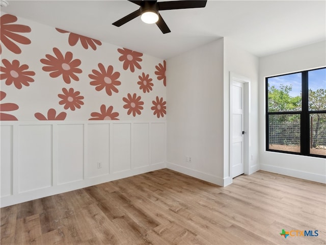 unfurnished bedroom with wallpapered walls, a wainscoted wall, wood finished floors, a decorative wall, and baseboards