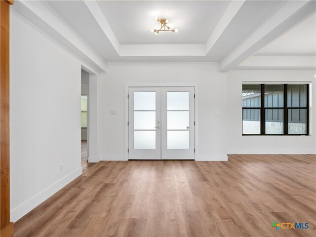interior space featuring a tray ceiling, light wood finished floors, baseboards, and french doors