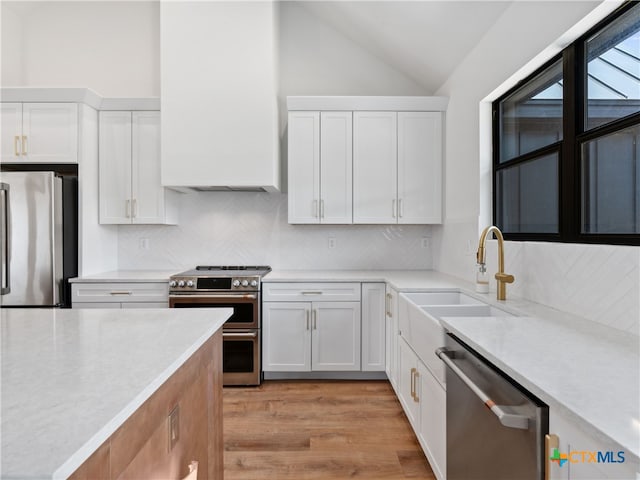 kitchen featuring white cabinets, lofted ceiling, light countertops, a sink, and appliances with stainless steel finishes