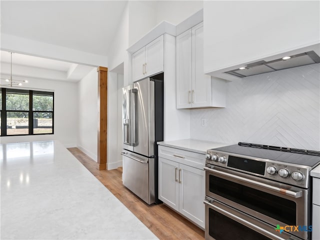 kitchen with white cabinets, light wood-style floors, backsplash, wall chimney range hood, and appliances with stainless steel finishes