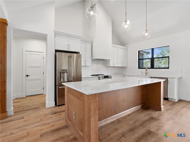 kitchen with white cabinets, light countertops, a kitchen island, appliances with stainless steel finishes, and high vaulted ceiling