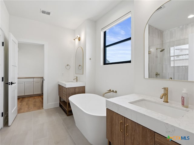 full bathroom with two vanities, a sink, tiled shower, visible vents, and a freestanding tub