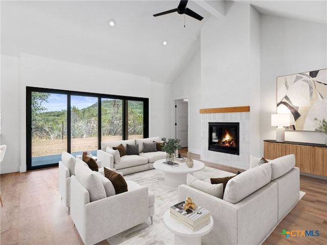 living room featuring light wood-type flooring, a tiled fireplace, beamed ceiling, a ceiling fan, and high vaulted ceiling