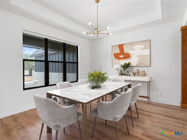 dining room with baseboards, light wood-style flooring, a tray ceiling, and a chandelier
