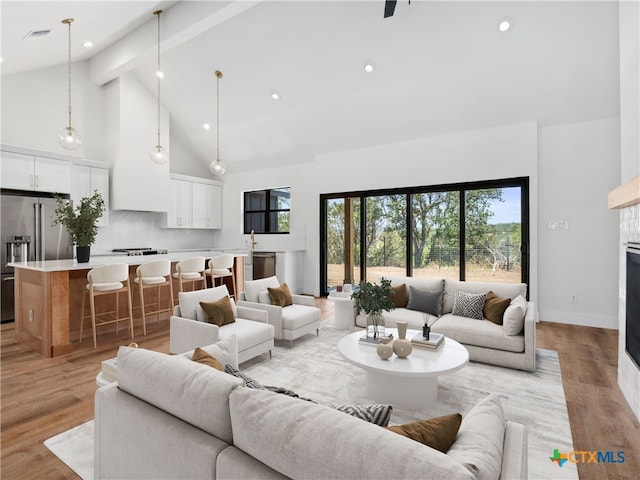 living area with light wood finished floors, a tiled fireplace, beam ceiling, and high vaulted ceiling
