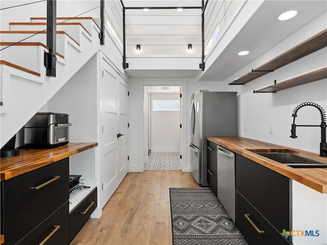 kitchen featuring open shelves, dark cabinetry, a sink, butcher block counters, and appliances with stainless steel finishes