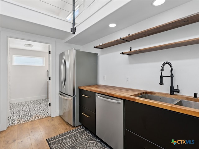 kitchen featuring open shelves, butcher block countertops, a sink, dark cabinetry, and stainless steel appliances