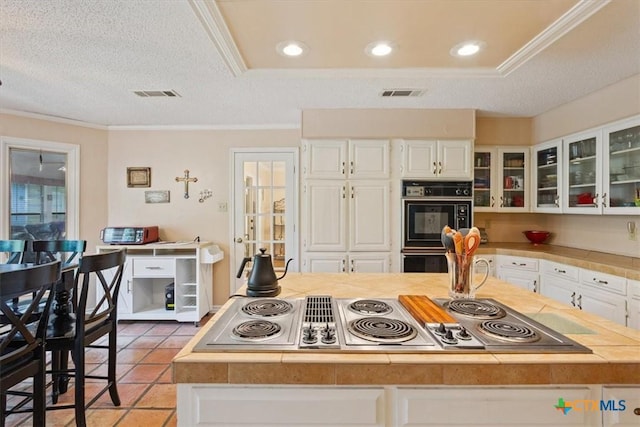 910 Mill Creek Dr, Salado, TX 76571 - kitchen featuring stainless steel electric stovetop, white cabinetry, crown molding, light countertops, and glass insert cabinets