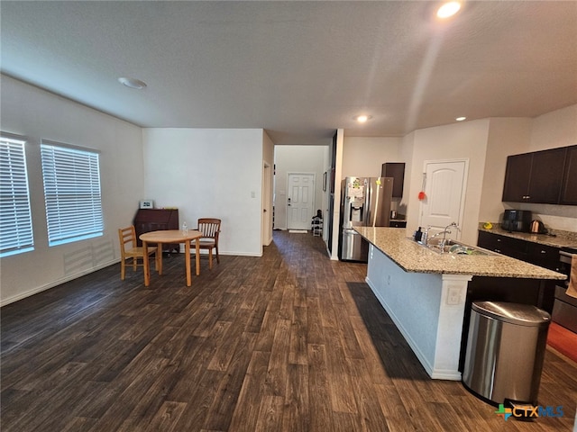 kitchen with sink, stainless steel fridge, an island with sink, dark brown cabinets, and dark hardwood / wood-style flooring