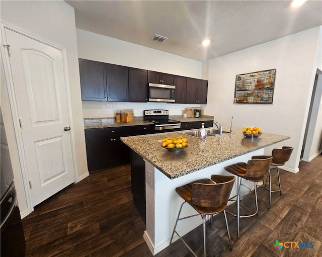 kitchen with a breakfast bar, a sink, visible vents, appliances with stainless steel finishes, and dark wood finished floors