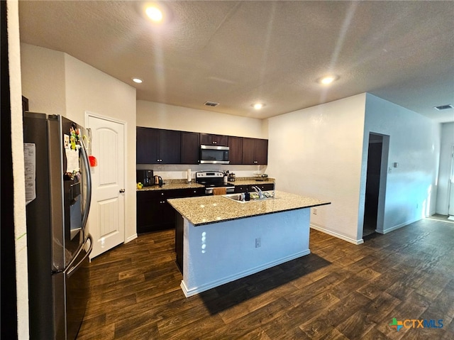 kitchen with dark brown cabinetry, stainless steel appliances, dark hardwood / wood-style flooring, a textured ceiling, and a center island with sink