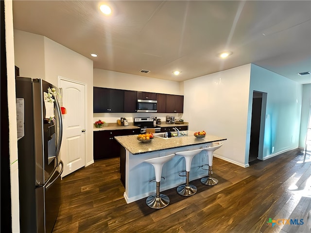 kitchen featuring a kitchen bar, a kitchen island with sink, appliances with stainless steel finishes, dark hardwood / wood-style flooring, and dark brown cabinetry