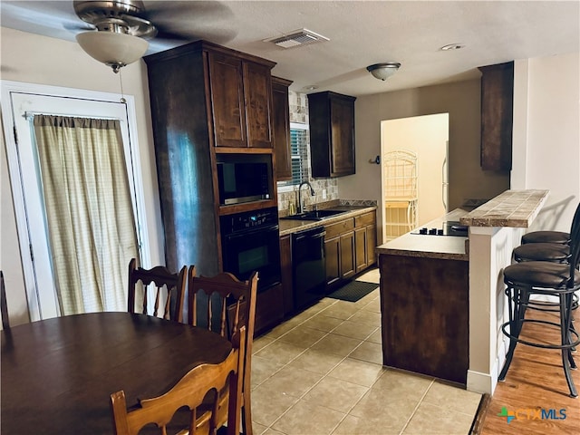 kitchen with sink, black appliances, a breakfast bar area, light tile patterned floors, and dark brown cabinets