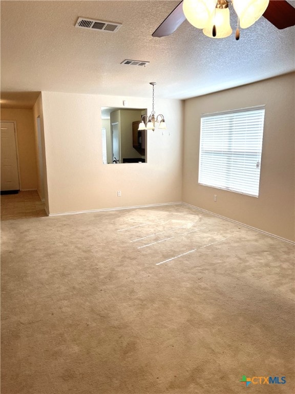 carpeted spare room featuring ceiling fan with notable chandelier and a textured ceiling