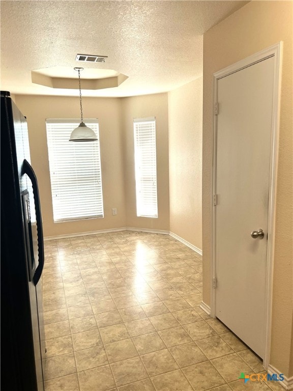 unfurnished dining area featuring a tray ceiling and a textured ceiling