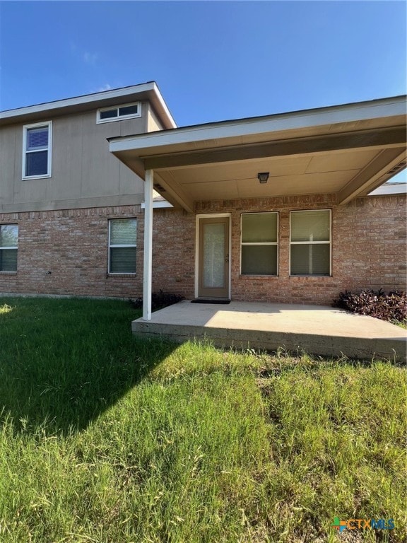 entrance to property featuring a patio area and a lawn