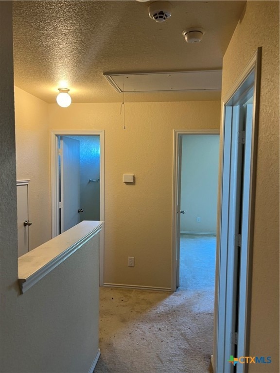 corridor with a textured ceiling and light carpet