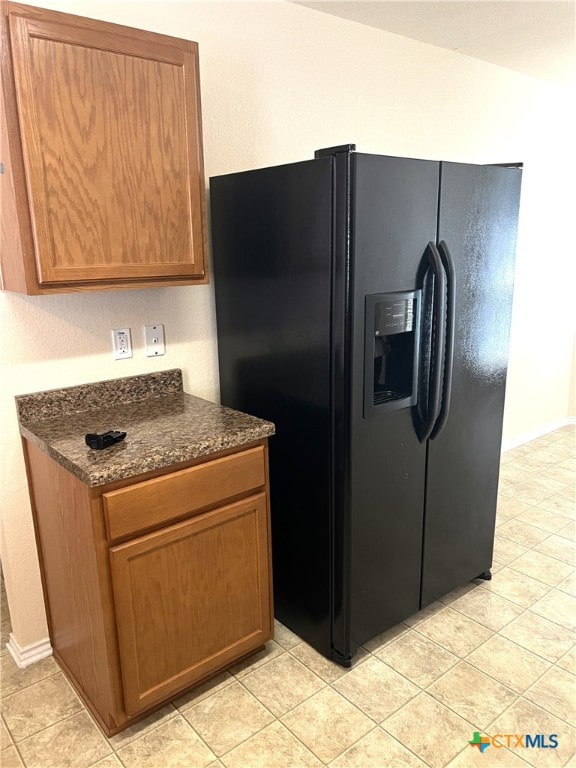 kitchen featuring dark stone countertops, black refrigerator with ice dispenser, and light tile patterned floors