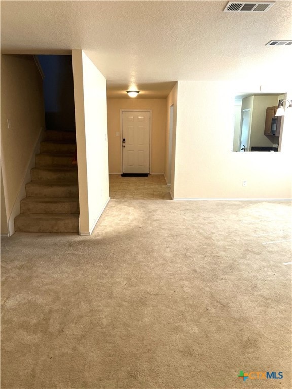 unfurnished living room with light colored carpet and a textured ceiling