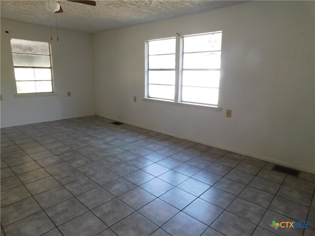 tiled empty room featuring ceiling fan, a textured ceiling, and a healthy amount of sunlight