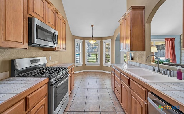 kitchen with appliances with stainless steel finishes, tile counters, sink, and light tile patterned floors