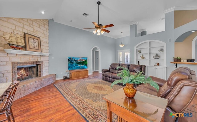 living room with vaulted ceiling, hardwood / wood-style floors, a fireplace, ceiling fan, and built in shelves