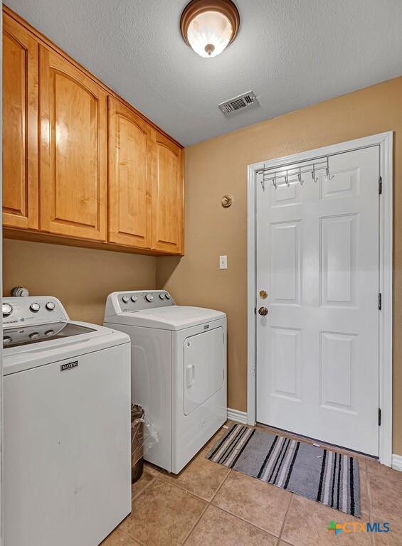 clothes washing area featuring cabinets, light tile patterned floors, a textured ceiling, and independent washer and dryer