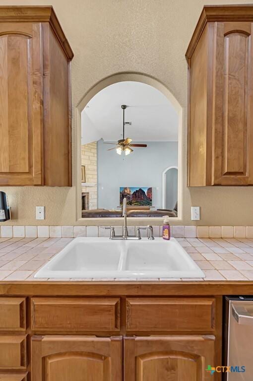 kitchen with sink, stainless steel dishwasher, tile counters, and ceiling fan