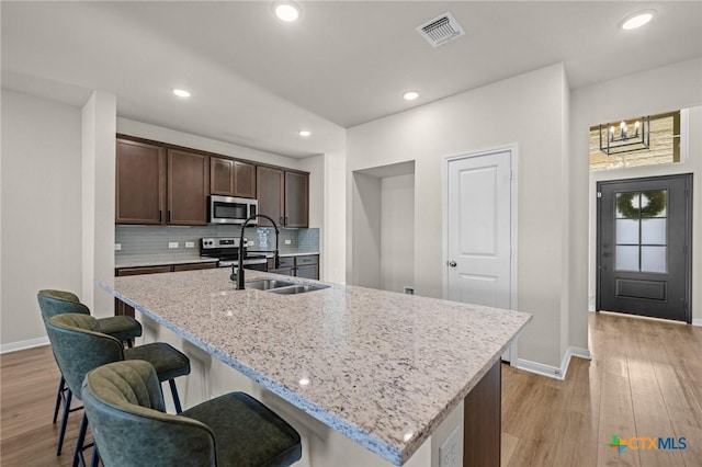 1821 Holleman Dr, Temple, TX 76502 - kitchen with appliances with stainless steel finishes, a breakfast bar area, light wood-style flooring, dark brown cabinetry, and recessed lighting