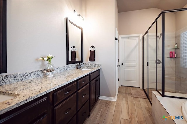 bathroom featuring vanity, a shower stall, wood finished floors, and vaulted ceiling